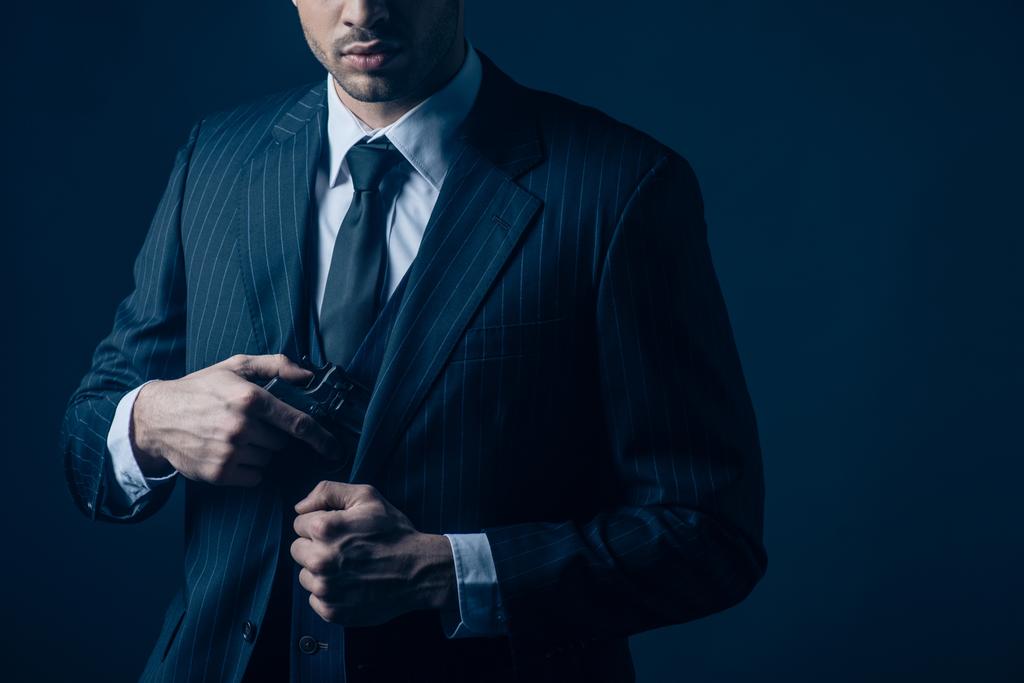 Ausgeschnittene Ansicht von Gangster versteckt Waffe im Anzug auf dunkelblauem Hintergrund - Foto, Bild