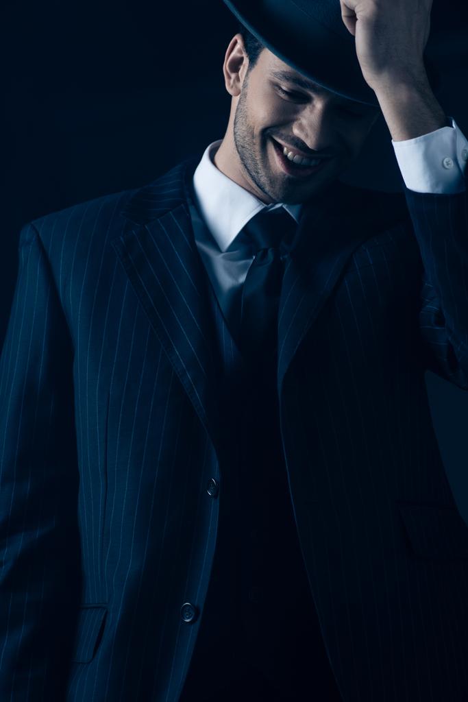 Vue de face du mafieux tenant un chapeau en feutre et riant sur fond sombre
 - Photo, image