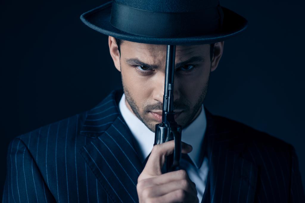 Portrait of gangster holding gun in front of face on dark blue - Photo, Image