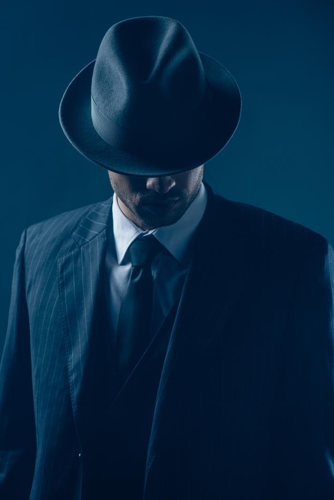 Μαφιόζο με καλυμμένα μάτια με καπέλο τσόχας σε σκούρο μπλε φόντο - Φωτογραφία, εικόνα