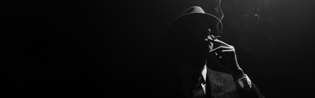 Monochrome image of mafioso silhouette smoking on black background, panoramic shot - Photo, Image
