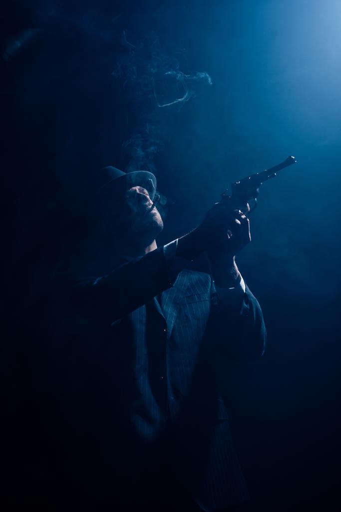 Silueta de gángster apuntando arma y humeante sobre fondo azul oscuro
 - Foto, imagen