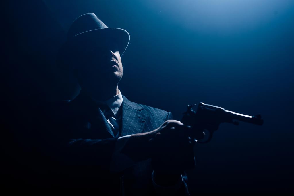Silhouette eines Mafioso mit ausgestreckten Händen, die auf dunklen Hintergrund zielen - Foto, Bild