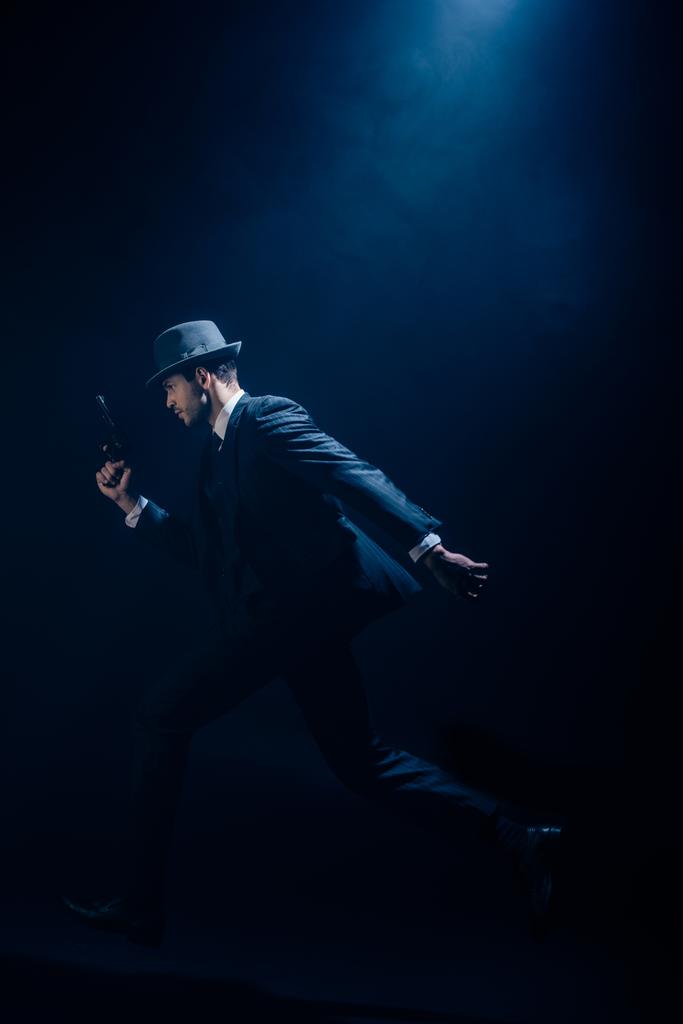 Gángster levantando la mano con pistola y corriendo sobre fondo azul oscuro
 - Foto, Imagen