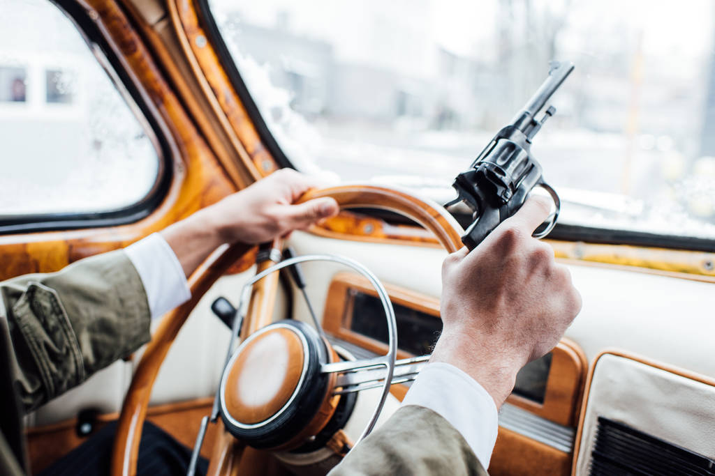 Vista cortada de mafioso segurando arma e carro de condução
 - Foto, Imagem