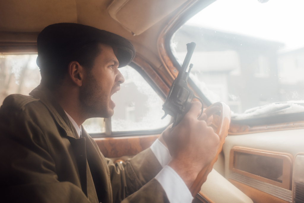 Προφίλ του ενοχλημένου γκάνγκστερ με όπλο φωνάζοντας και οδηγώντας αυτοκίνητο - Φωτογραφία, εικόνα