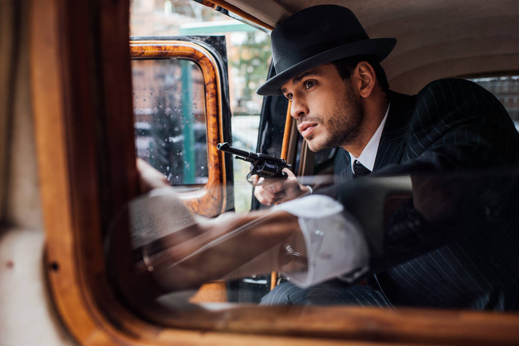 Вибірковий фокус гангстера, що сидить в засідці з пістолетом в ретро-автомобілі
 - Фото, зображення
