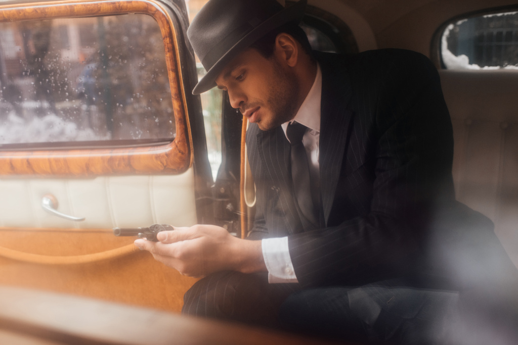 Mafioso sieht Revolver in Händen, während er im Auto sitzt - Foto, Bild