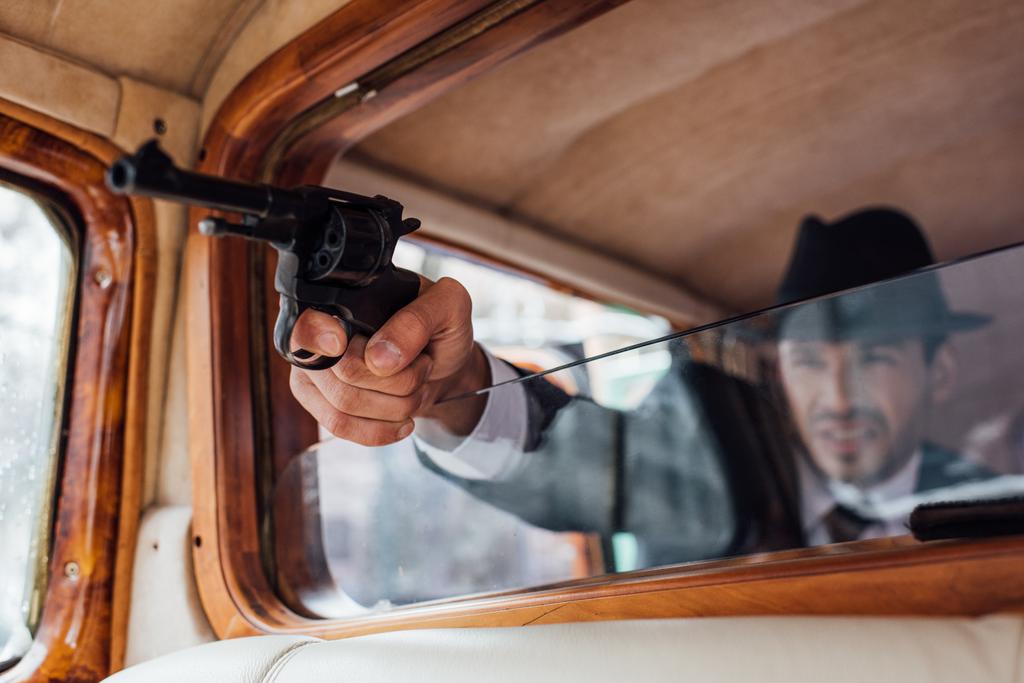 Valikoiva painopiste gangsteri tähtäävä ase ojensi kätensä retro auton
 - Valokuva, kuva
