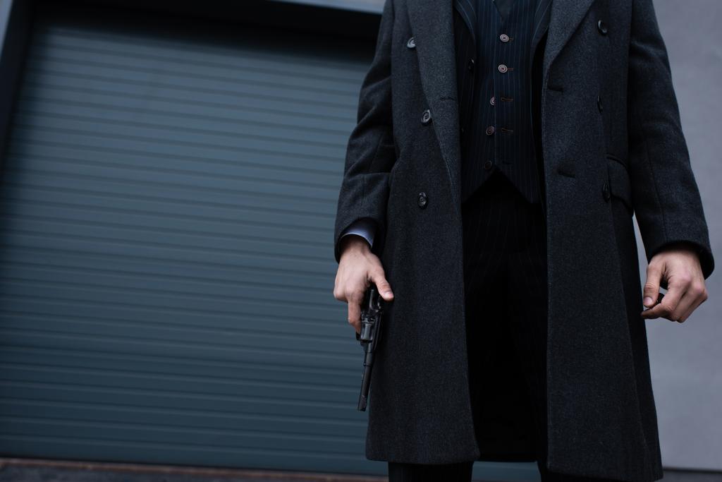 Vista recortada de gangster en abrigo negro con pistola en la calle
 - Foto, Imagen