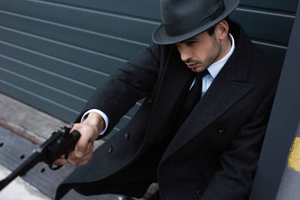 Selektivní zaměření mafiána s nataženou rukou mířící zbraň blízko zdi na ulici - Fotografie, Obrázek