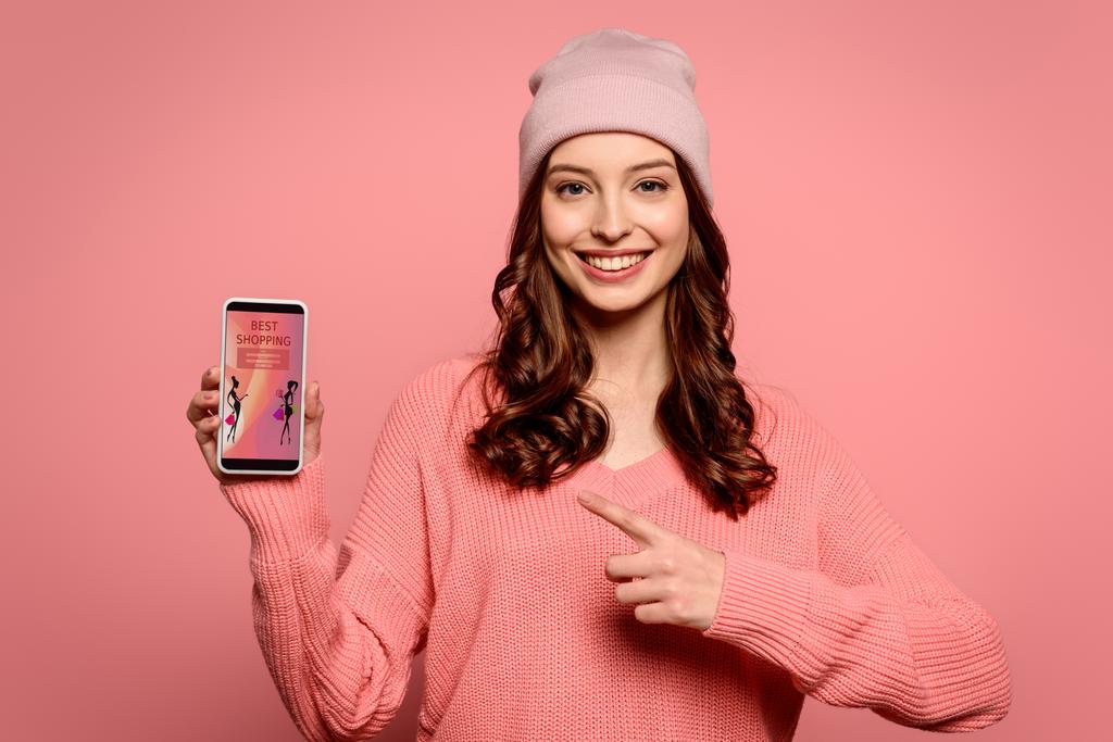 gelukkig meisje wijzen met de vinger naar smartphone met de beste shopping app op het scherm geïsoleerd op roze - Foto, afbeelding