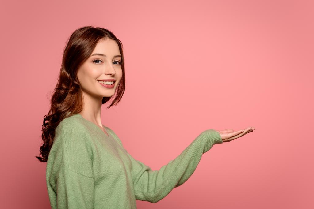 веселая девушка улыбается в камеру, стоя с открытой рукой изолированы на розовый
 - Фото, изображение