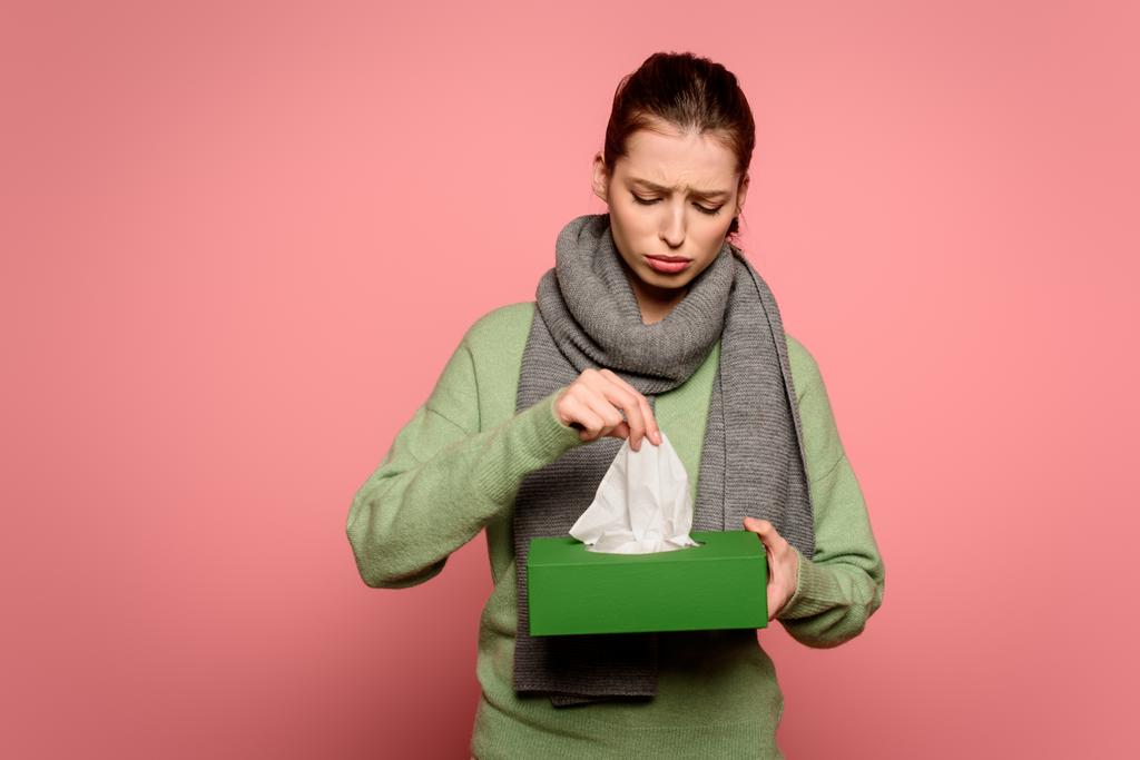 rozrušený, nemocná dívka v teplém šátku přičemž papírový ubrousek z krabice na růžovém pozadí - Fotografie, Obrázek