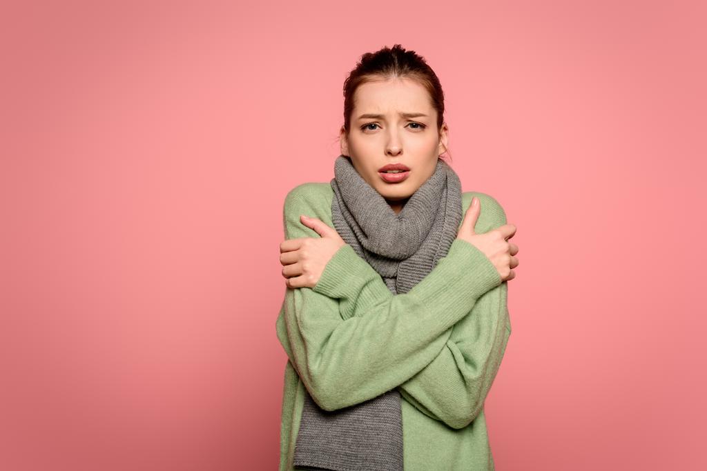 ziek meisje in warme sjaal knuffelen zichzelf terwijl het hebben van koorts geïsoleerd op roze - Foto, afbeelding
