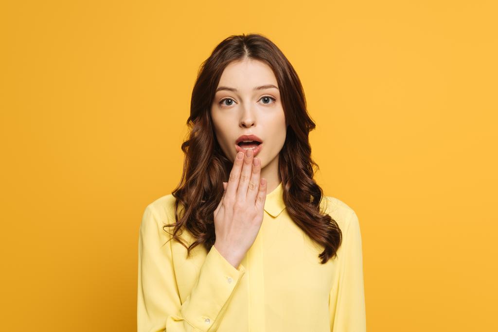 chocada chica sosteniendo la mano cerca de la boca abierta mientras mira a la cámara aislada en amarillo
 - Foto, imagen