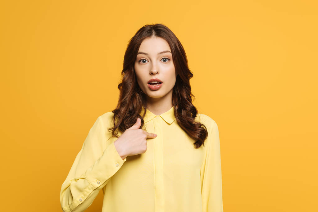 surprised girl pointing with finger at herself while looking at camera  isolated on yellow - Photo, Image