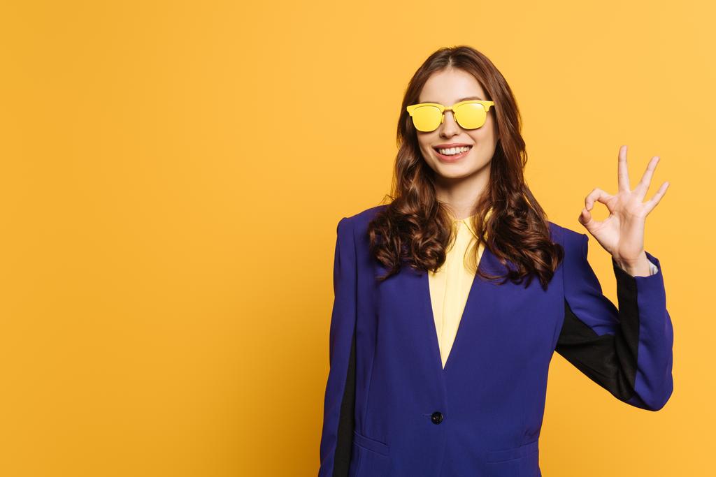 boldog, elegáns lány sárga szemüvegben mutatja rendben gesztus elszigetelt sárga - Fotó, kép