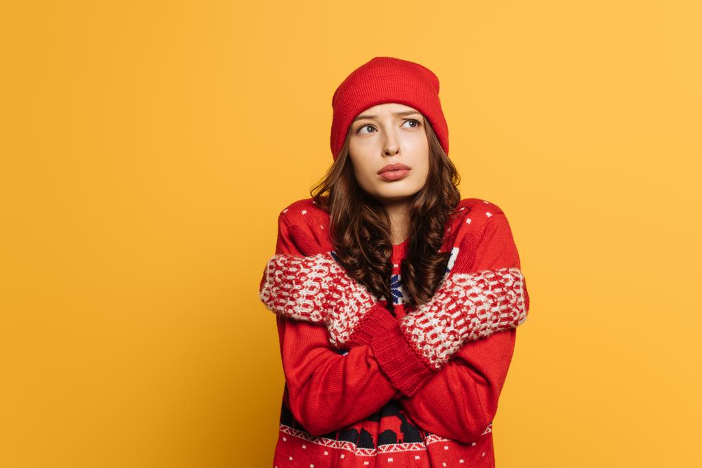chica disgustada en suéter ornamental rojo y manoplas abrazándose mientras se siente fría aislada en amarillo
 - Foto, imagen