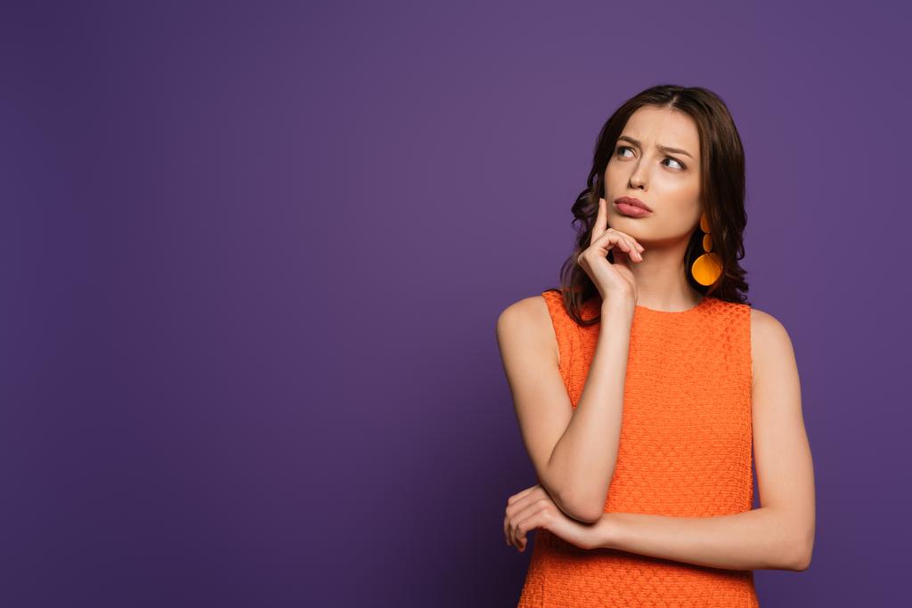 thoughtful girl looking away while touching face on purple background - Photo, Image