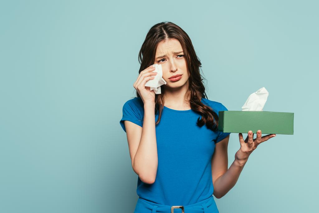Грустная девушка вытирает слезы бумажной салфеткой, плача изолированно на синий
 - Фото, изображение