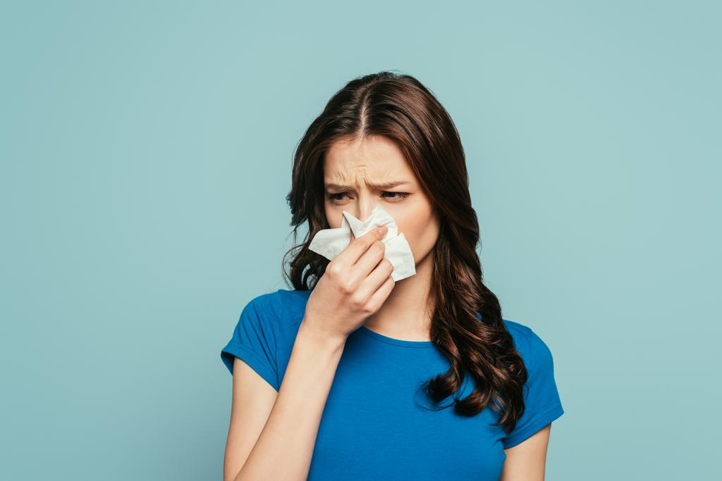 αναστατωμένο, άρρωστο κορίτσι σκουπίζει τη μύτη με χαρτοπετσέτα απομονωμένη στο μπλε - Φωτογραφία, εικόνα