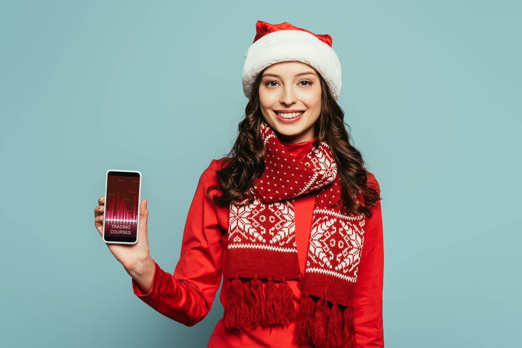 веселая девушка в шляпе Санта показывает смартфон с цифровым приложением анализов на экране на синем фоне
  - Фото, изображение