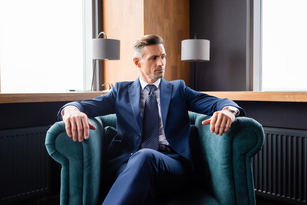 бизнесмен в костюме сидит в кресле и смотрит в сторону
  - Фото, изображение