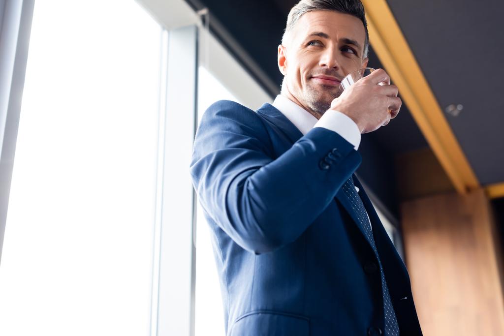 nízký úhel pohledu usměvavý podnikatel v obleku drží sklo  - Fotografie, Obrázek