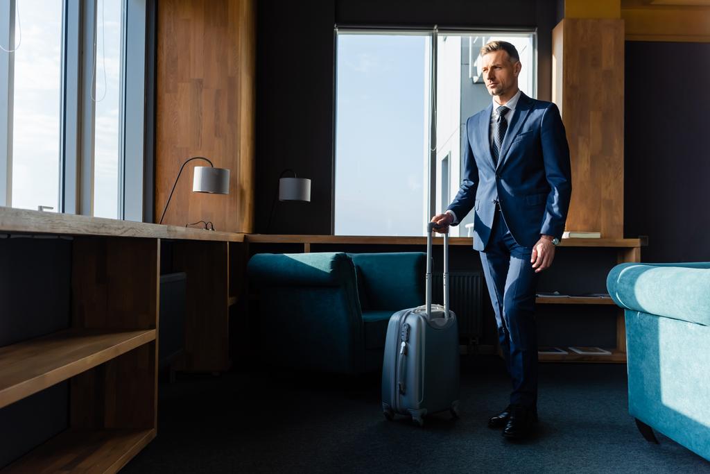 hombre de negocios guapo de traje caminando con bolsa de viaje en el hotel
  - Foto, imagen
