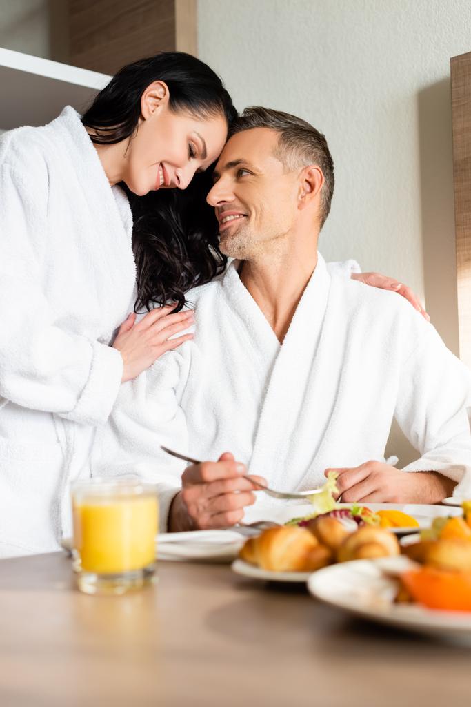 foyer sélectif de petite amie souriante en peignoir étreignant petit ami pendant le petit déjeuner
  - Photo, image
