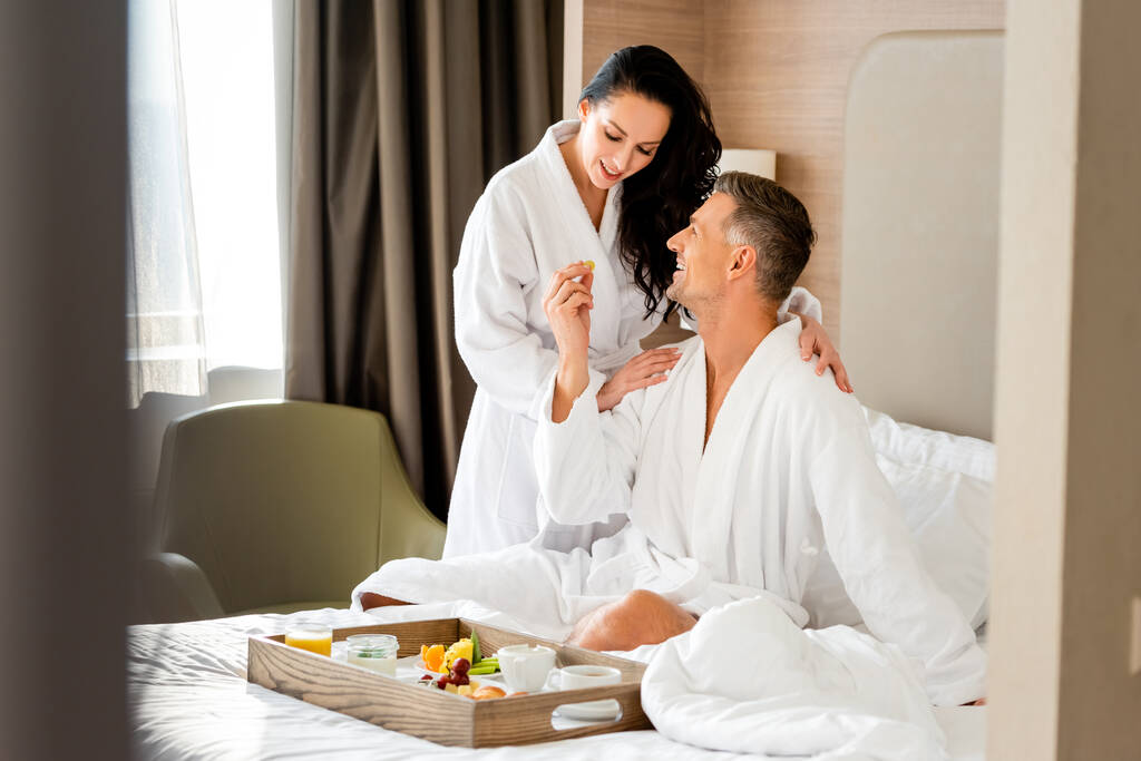 Lächelnder Freund füttert attraktive Freundin im Hotel mit Trauben  - Foto, Bild