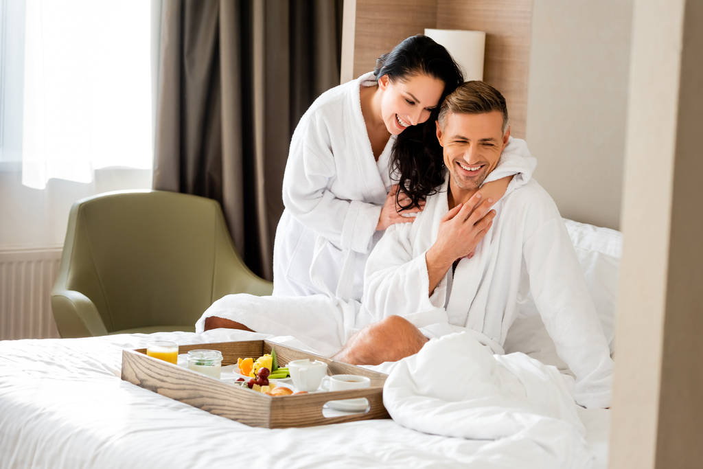 smiling girlfriend in bathrobe hugging handsome boyfriend in hotel  - Photo, Image