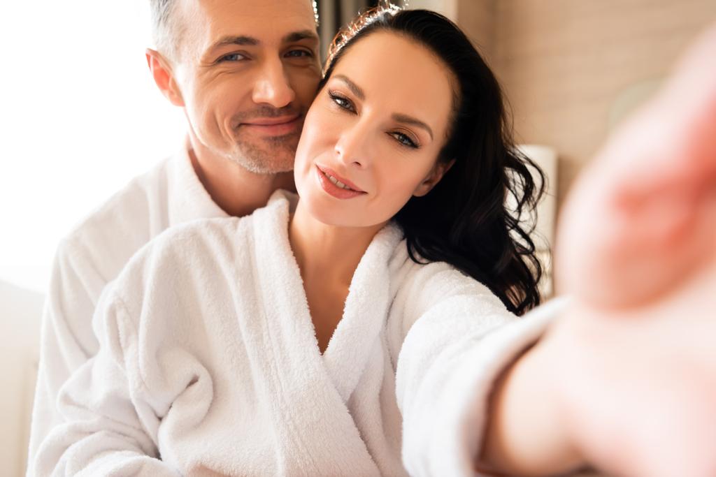 селективный фокус улыбающейся девушки, делающей селфи с парнем в отеле
 - Фото, изображение