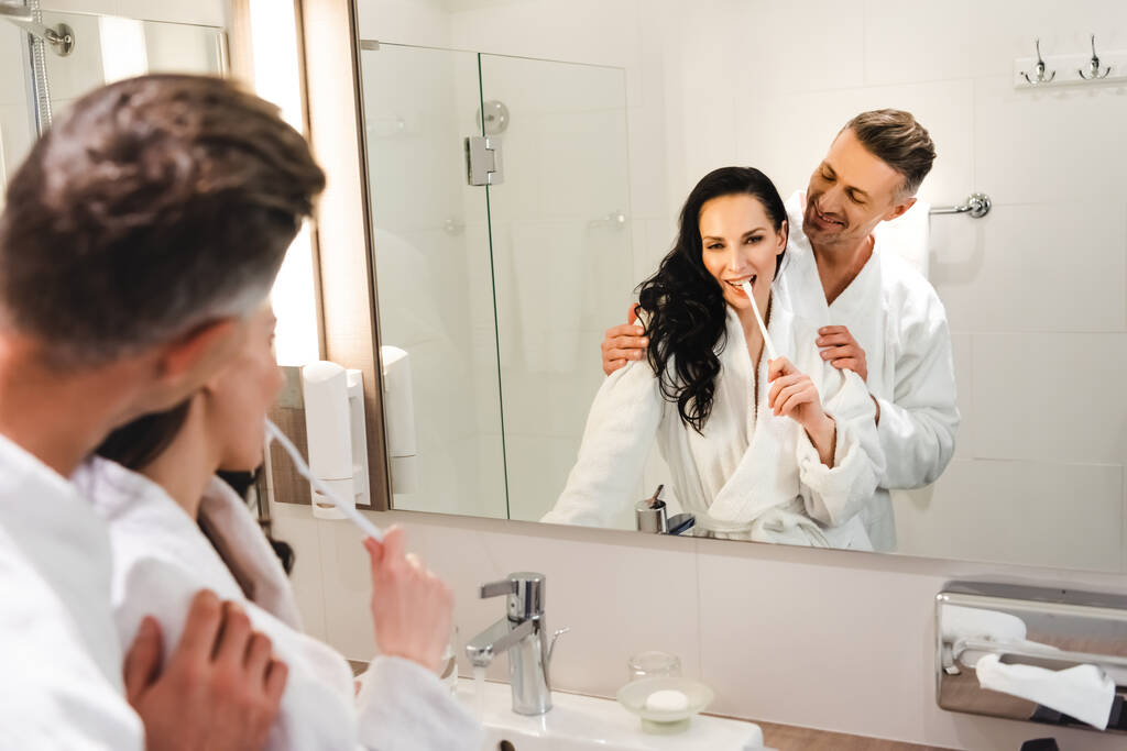 enfoque selectivo de novio abrazando novia sonriente y ella cepillándose los dientes en el hotel
 - Foto, imagen