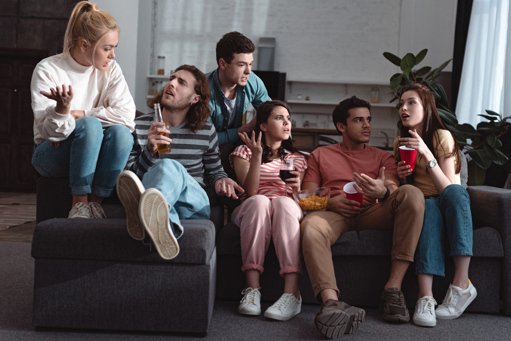 mladí přátelé mluví a gesta, zatímco sedí na pohovce doma - Fotografie, Obrázek
