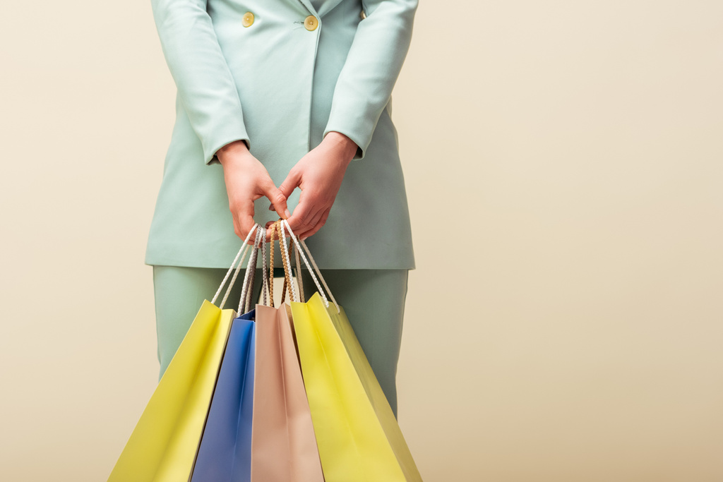 cropped view of young woman holding shopping bags isolated on beige  - Photo, Image