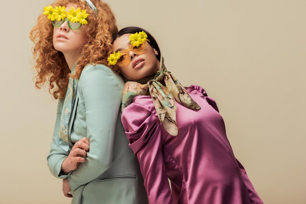 élégante fille afro-américaine et femme bouclée dans des lunettes de soleil avec des fleurs posant isolé sur beige
 - Photo, image