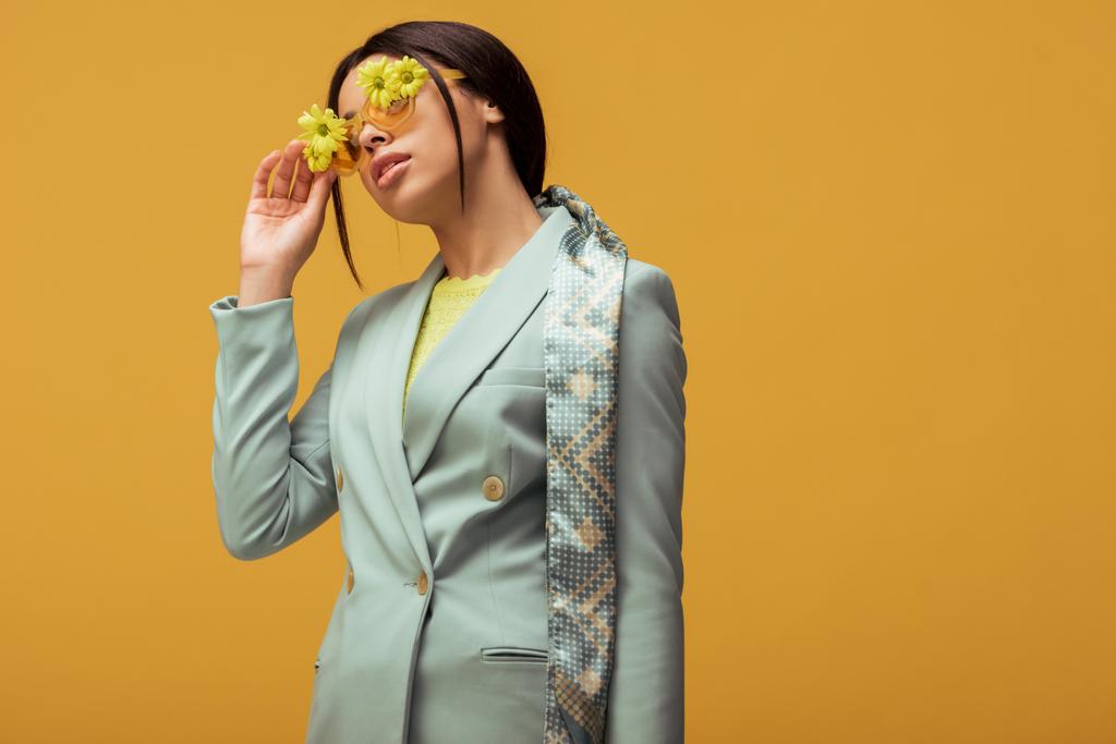 trendy african american girl in suit and scarf touching sunglasses with flowers isolated on yellow  - Photo, Image