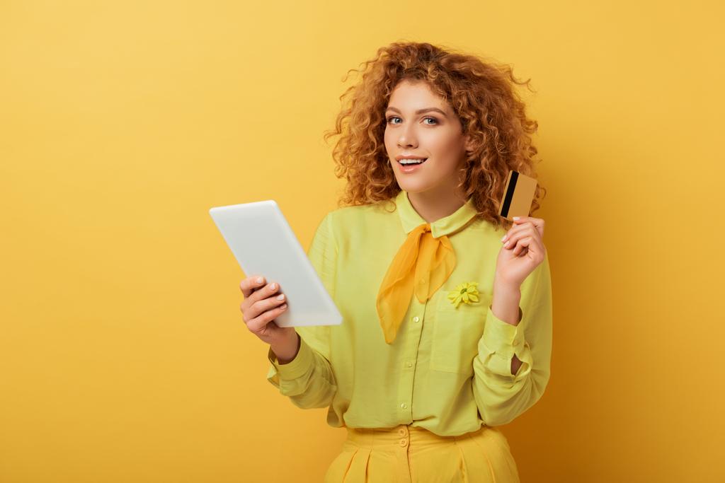 fröhliches rothaariges Mädchen mit digitalem Tablet und Kreditkarte auf gelb  - Foto, Bild