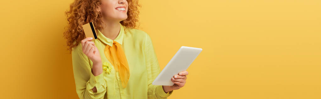 panoráma lövés vidám vörös hajú nő kezében digitális tabletta és hitelkártya sárga  - Fotó, kép