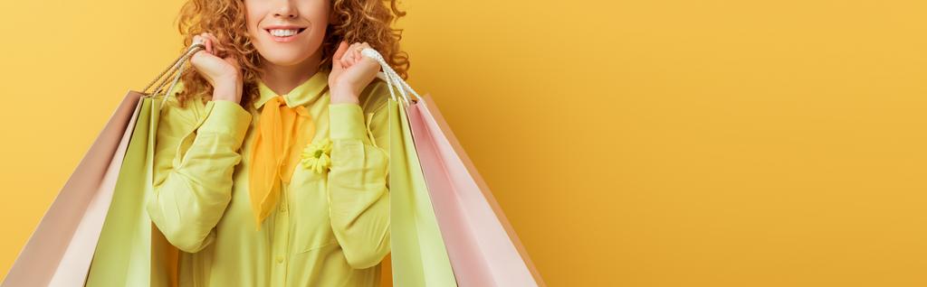 tiro panorámico de la pelirroja feliz sosteniendo bolsas de compras en amarillo
  - Foto, Imagen
