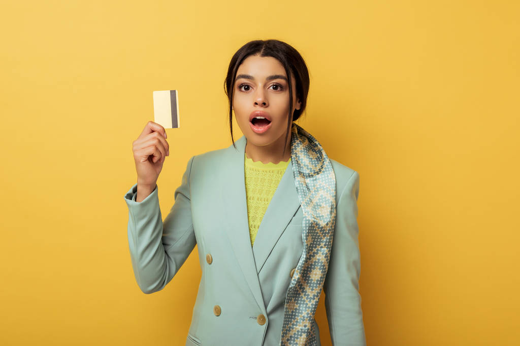 surprised african american girl looking at camera and holding credit card on yellow  - Photo, Image