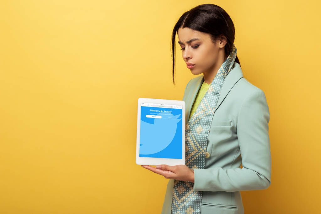 displeased african american woman holding digital tablet with twitter app on yellow  - Photo, Image