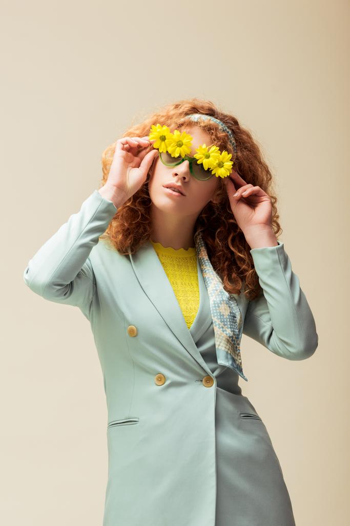 tyylikäs punapää nainen puku koskettaa aurinkolasit kukkia poseeratessaan eristetty beige
  - Valokuva, kuva