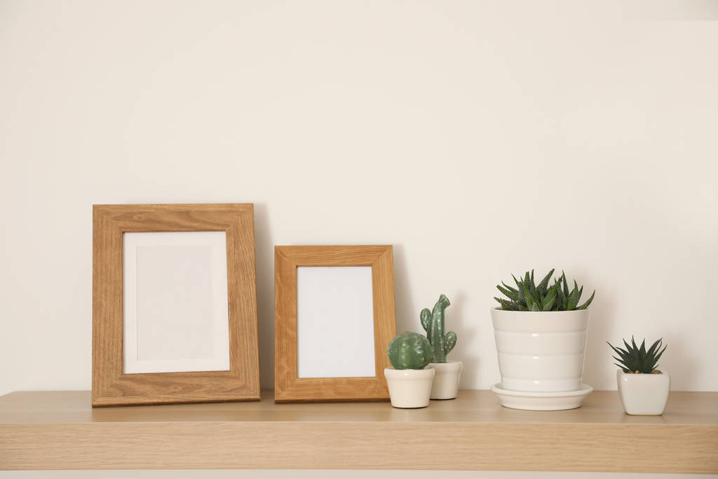 Wooden shelf with houseplants and photo frames on light wall - Photo, Image