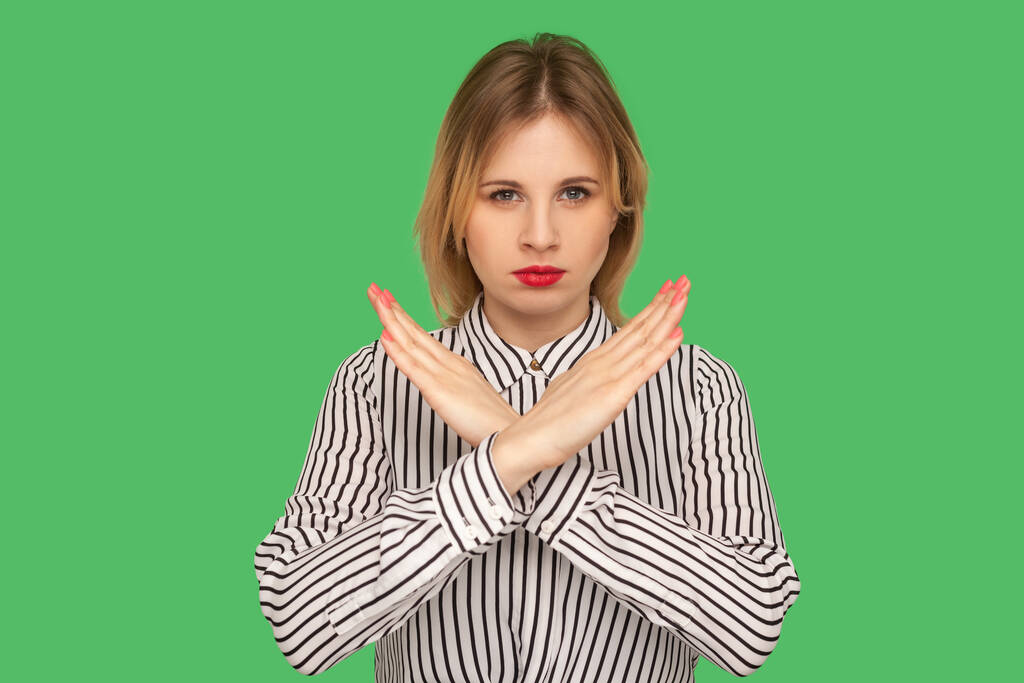 Ні в якому разі! Серйозна дівчина з червоними губами в смугастій блузці, що стоїть з схрещеними руками, жестикулює стоп, закінчується, показує символ відторгнення, мови тіла. критий студійний знімок ізольований на зеленому фоні
 - Фото, зображення