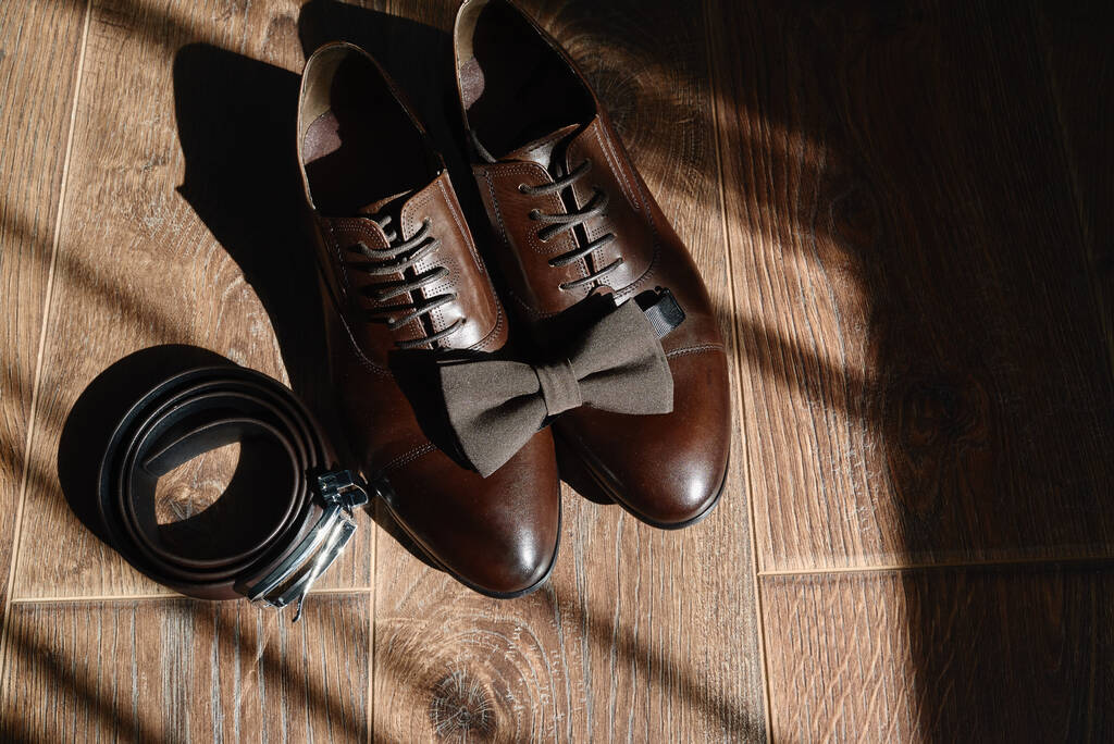 Cierre de zapatos masculinos marrones, corbata y cinturón en el fondo del piso de madera, espacio de copia. Accesorios hombre moderno. Detalles de la boda. Vista superior, plano
 - Foto, imagen