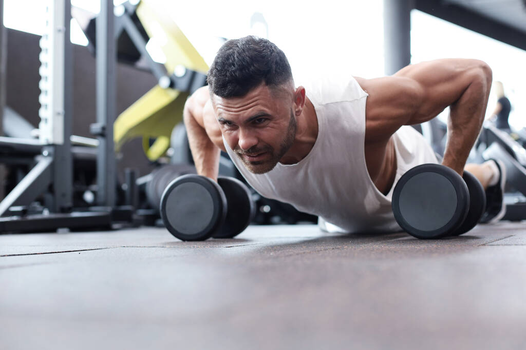 Spor salonunda dambıllarla yatay şınav yapan fit ve kaslı adam - Fotoğraf, Görsel
