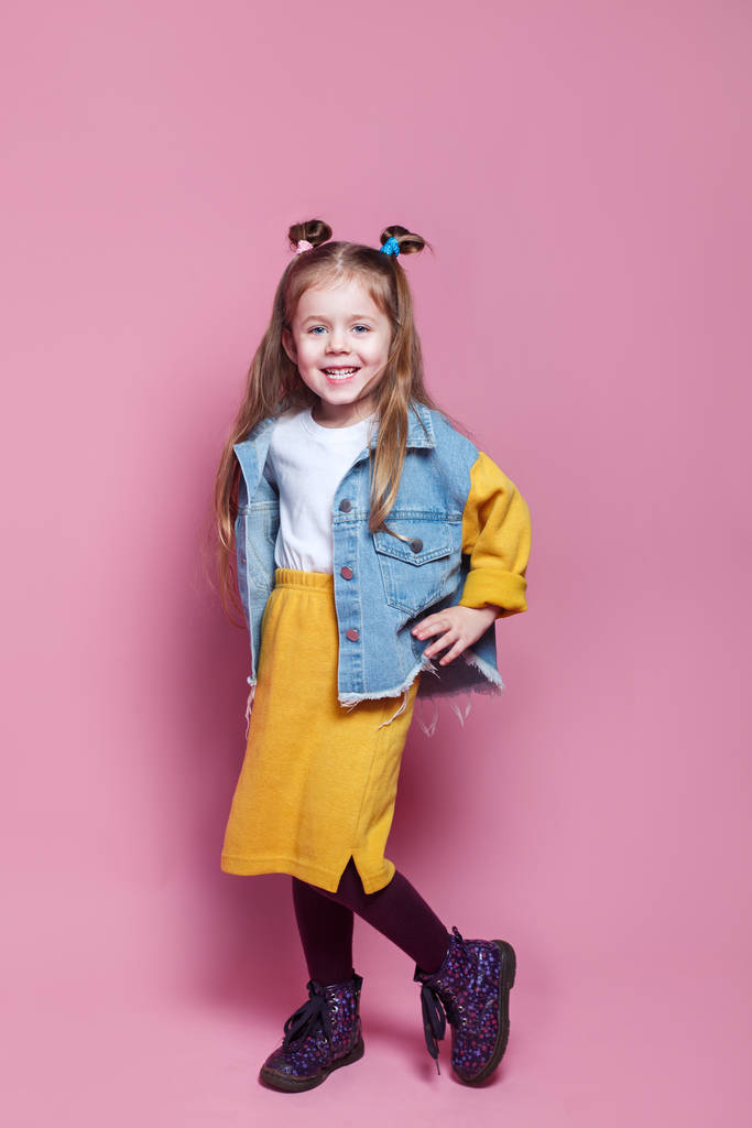 Täyspitkä muotokuva söpö pieni lapsi tyttö tyylikäs farkut vaatteet katselee kameraa ja hymyilee
 - Valokuva, kuva